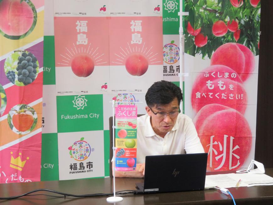桃のイラストが描かれた幟が置いてあるバックパネルの前で、市長がノートパソコンの画面を見ている写真