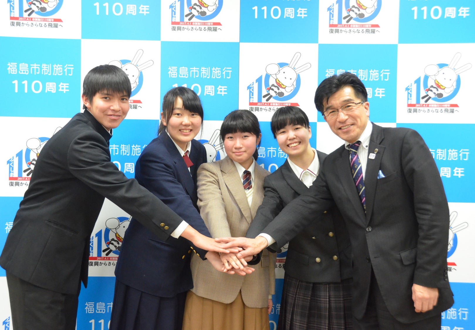 バックパネルの前で、市長と高校生4人が手を合わせている写真