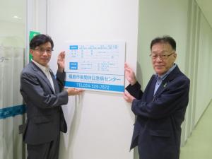 市長と男性が壁に設置されたプレート看板に手を添えている写真