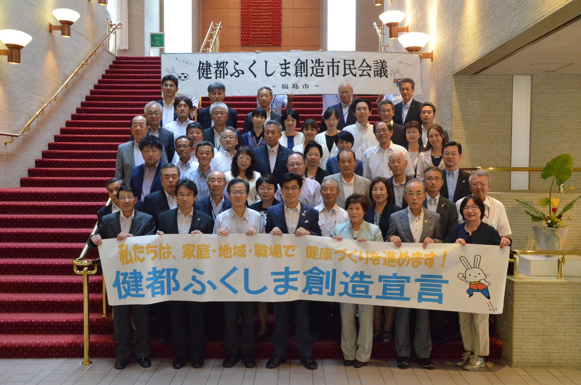 階段に市長と保健・医療機関や経済団体、地域の団体などの方々が並び、前列で市長と「健都ふくしま創造宣言」と書かれた横断幕を持ち記念撮影している写真