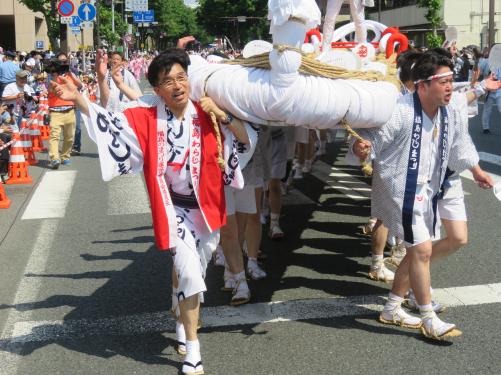 巨大な大わらじを肩に担いで道路を歩く市長と参加者の写真