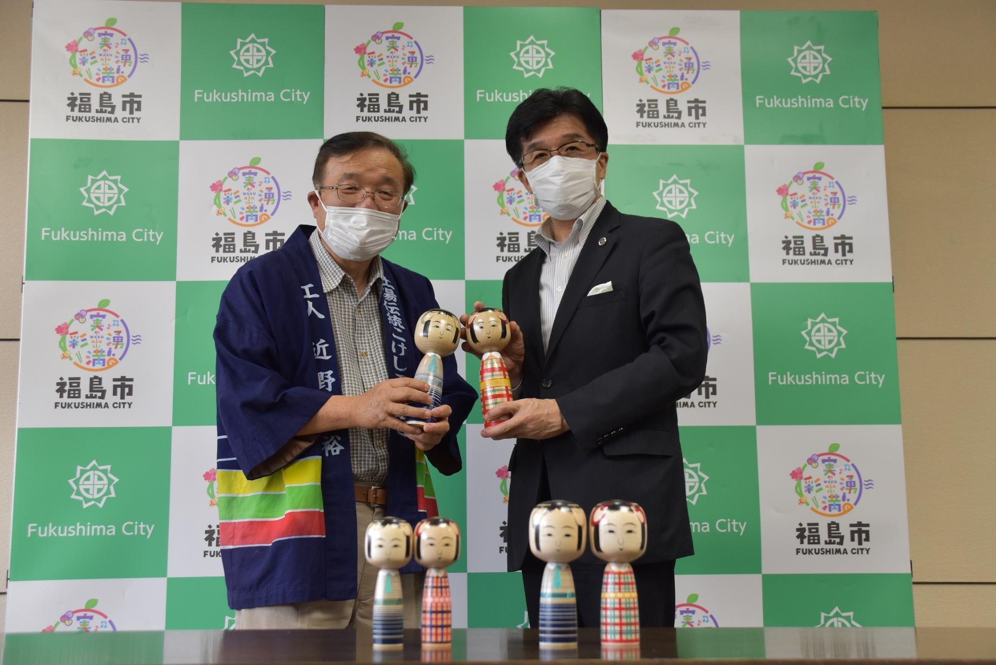 福島市のバックボードの前で市長と半被をきた男性がこけしをもって記念撮影している写真