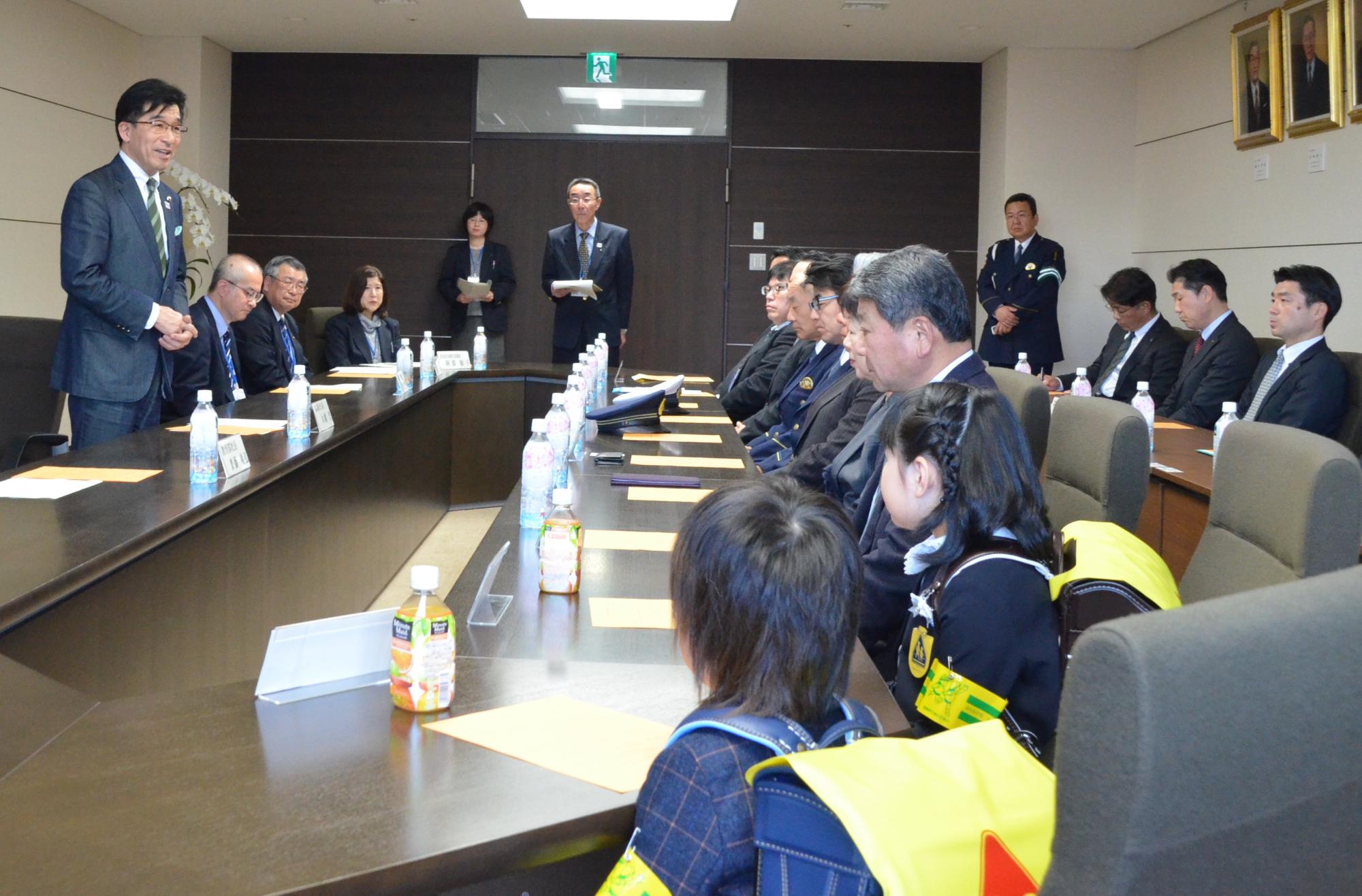 市長応接室で、市長が席に座っている小学生と関係者に向けて話をしている写真