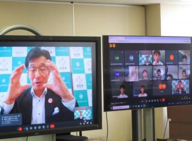 バックパネルの前にいる市長を映しているモニターと各児童が分割して映しているモニターを撮影した写真