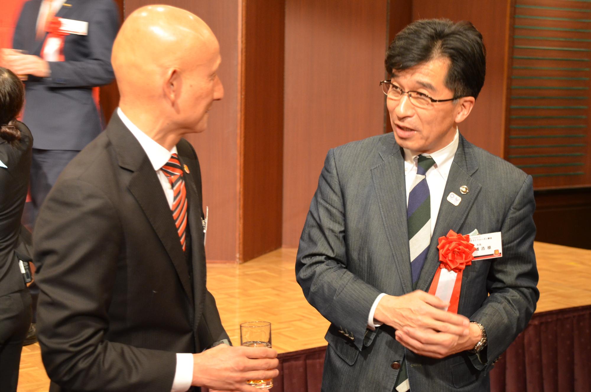 グラスを持った田坂監督と胸章をつけた市長が話をしている写真