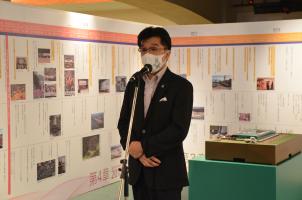 写真や復興の歩みが壁のパネルに展示された会場で、マイクスタンドの前に立つ市長の写真