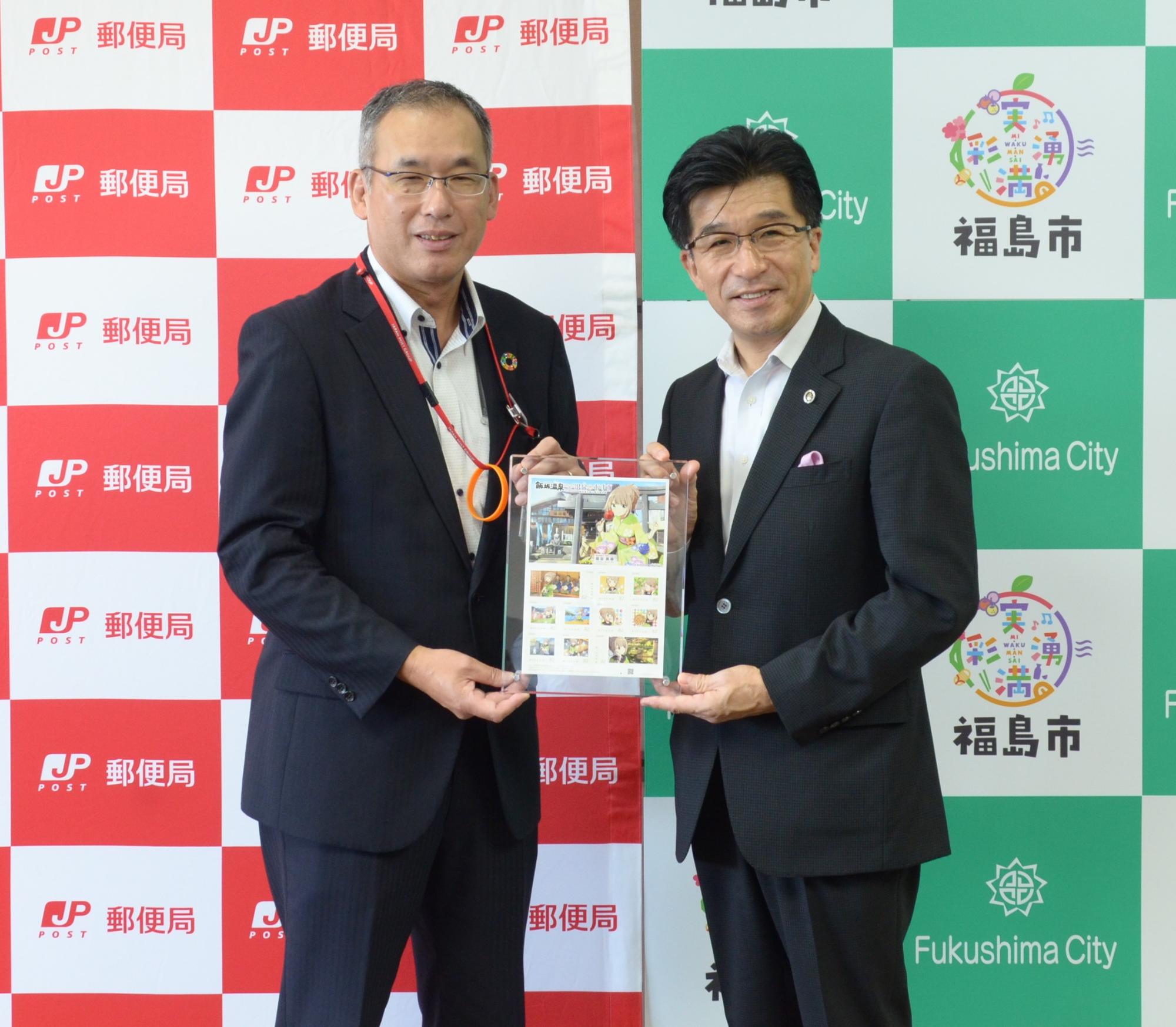 日本郵政と福島市のバックボードの前で日本郵便株式会社古屋正昭東北支社長から、オリジナルフレーム切手の贈呈を受ける市長の写真