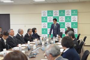 前方に設置された福島市のバックボードの前に市長が立って話しているのを向かい合って設置された長机に座って話を聞いている関係者の写真