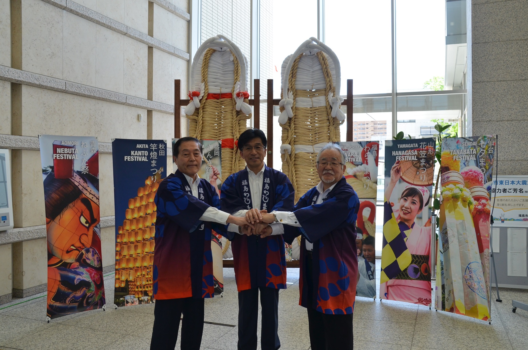 長さが3メートルほどの紅白の大わらじの前で市長と男性2人が手を真ん中で握り合い記念撮影している写真