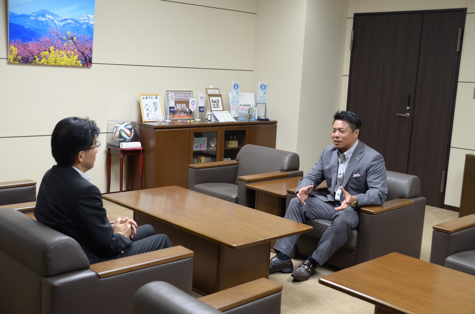 応接室で市長と岩村明憲監督が向かい合わせに座り談笑している写真