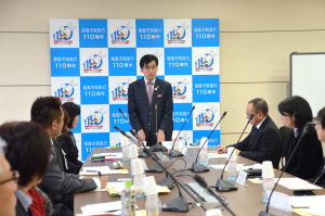 バックパネルの前に市長が立ち話す様子を、向かい合って座っている参加者たちが話を聞いている写真