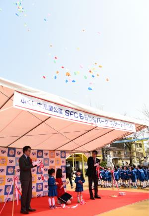 「ふくしま児童公園SFCももりんパークスタートイベント」と書かれた横断幕が掲げられたテントの下に赤いカーペットが敷かれ、テントの中で制服を着た小さい女の子2人と市長、関係者の男性によるテープカットが行われている様子の写真