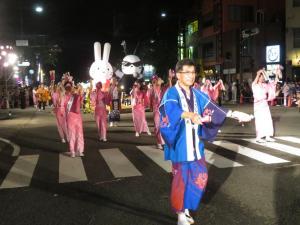 夜の道路を祭りの衣装を着た市長や大勢の人が歩き、後ろにはうさぎのキャラクターが見えている写真