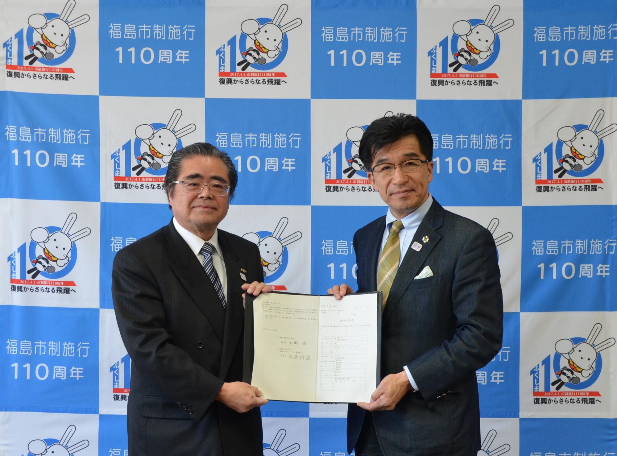 バックパネルの前で市長と男性が協定書を二人で手に持っている写真