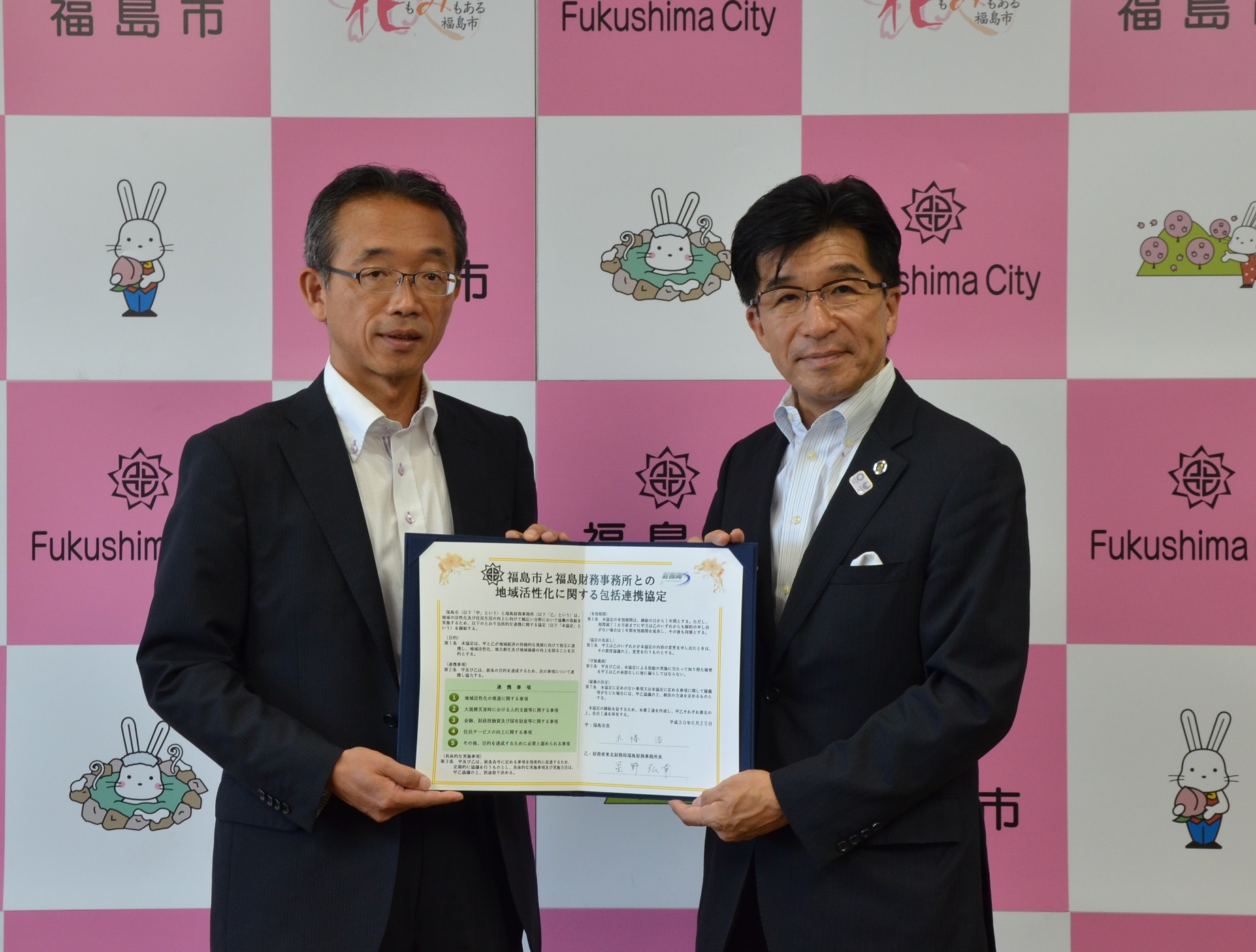 バックパネルの前で市長と関係者が、締結書を開き、2人で手に持っている写真