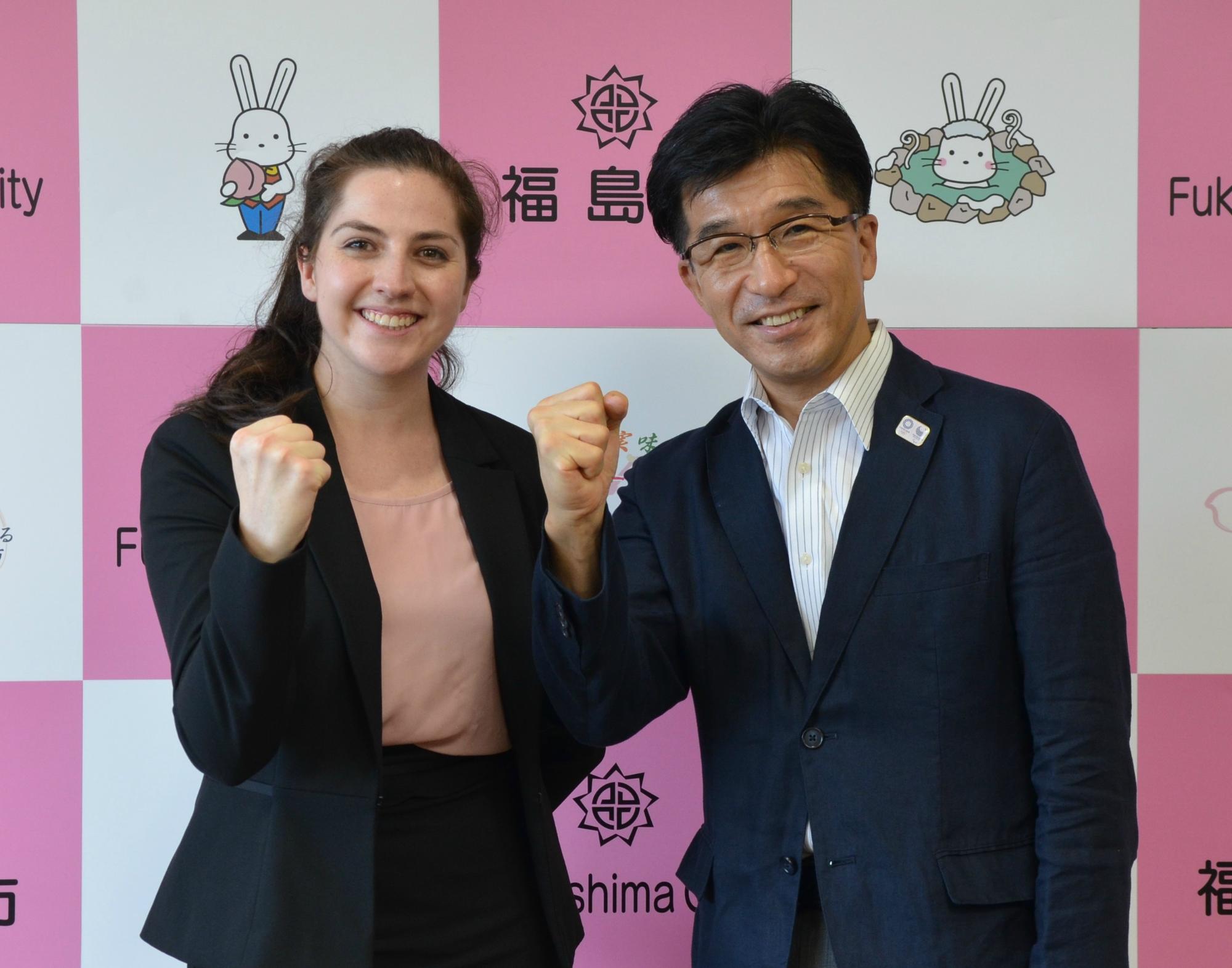 福島市のバックパネル前で、オーストラリア出身のルイス・アデル・キャロルさんと市長が握りこぶしでポーズを取っている写真
