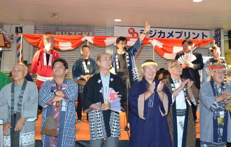 はっぴ姿の市長と関係者が2列で並んでおり、市長が腕を上げてマイクで話をしている写真