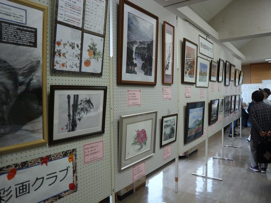 たくさんの額にはいった絵画や写真の作品が展示され、見学者がみている文化祭での写真