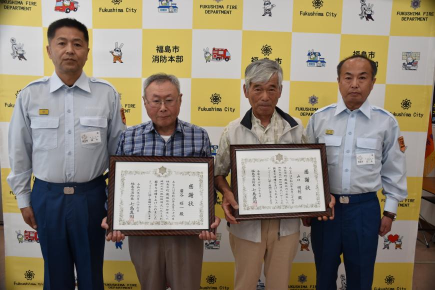 廣谷昭一さん、山口明利さんが感謝状を持って消防本部橋本次長、七島消防長で記念写真