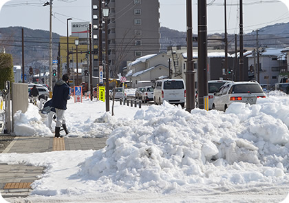 歩道に積もった雪を人が除雪する写真