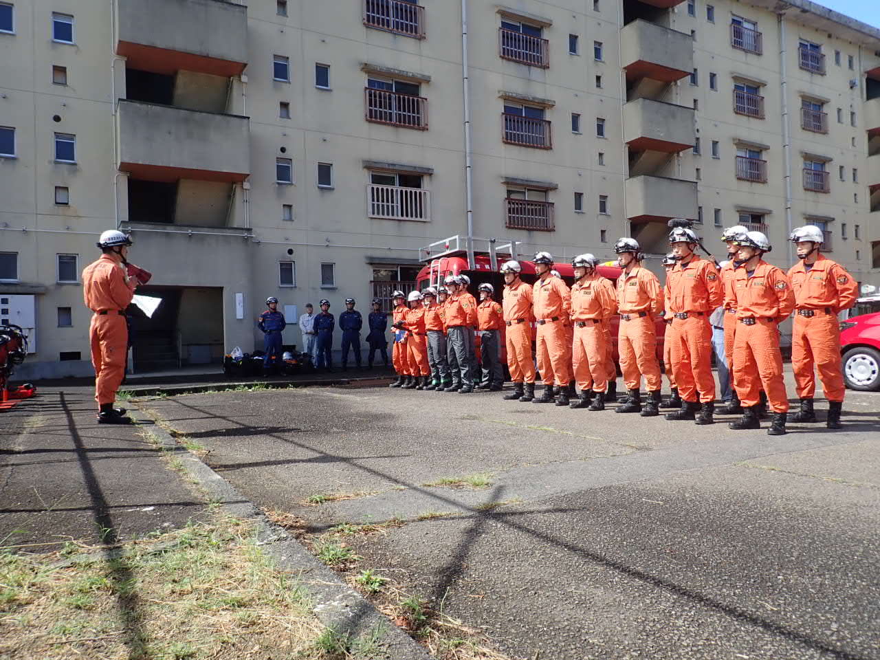 訓練に参加した3消防本部の救助隊員約30名が2列に整列し、救助隊長の指示を聞いている写真
