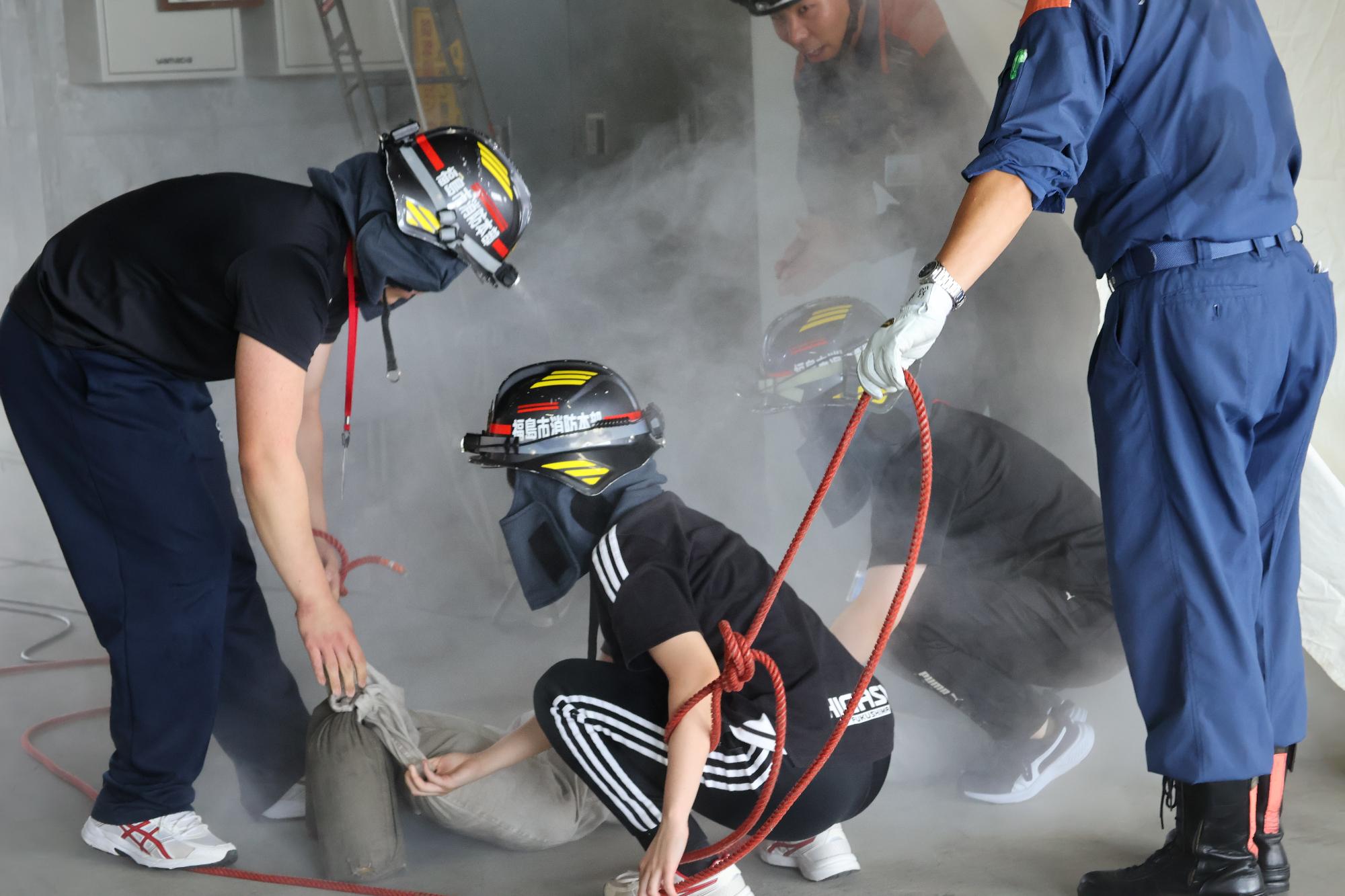 参加者3名がヘルメットをかぶり、訓練用の白煙が充満しているテント内から訓練人形を救出している写真