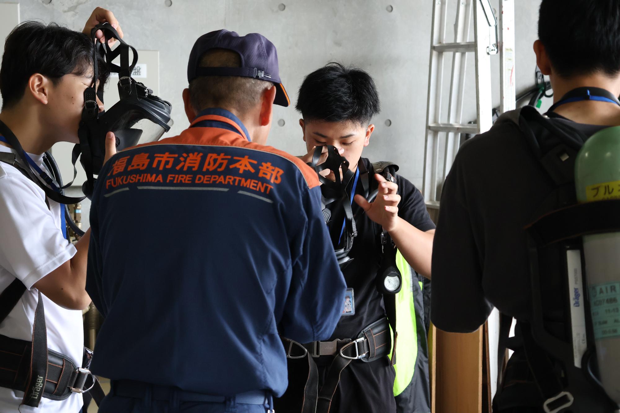 消防士の指導のもと参加者が空気呼吸器を背負い、面体を装着している写真