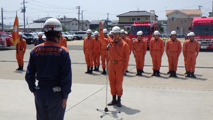 オレンジ色の消防服を着てヘルメットを着用した消防隊員が整列し、隊員の代表1名が選手宣誓をしている様子の写真