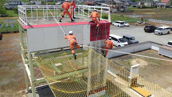 隊員1名が空中に張られたロープを渡り、奥では別の意隊員が2名ロープを伝い降下する訓練をしている様子の写真