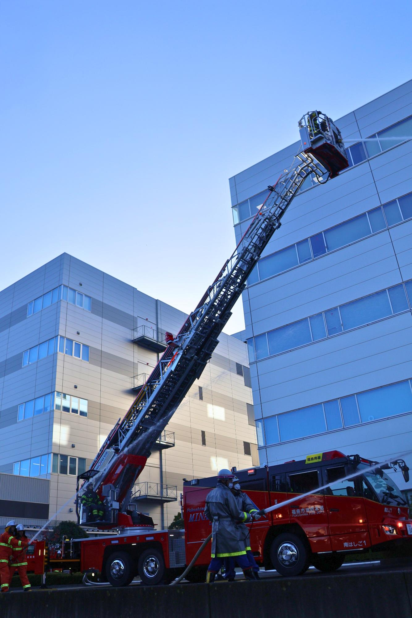 陸上自衛隊、地元消防団の隊員とはしご車が一斉に放水している写真