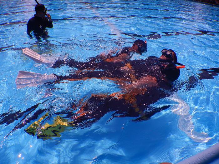 プールの水面上で水難救助隊員2名が溺者役の男性を曳航する訓練の様子