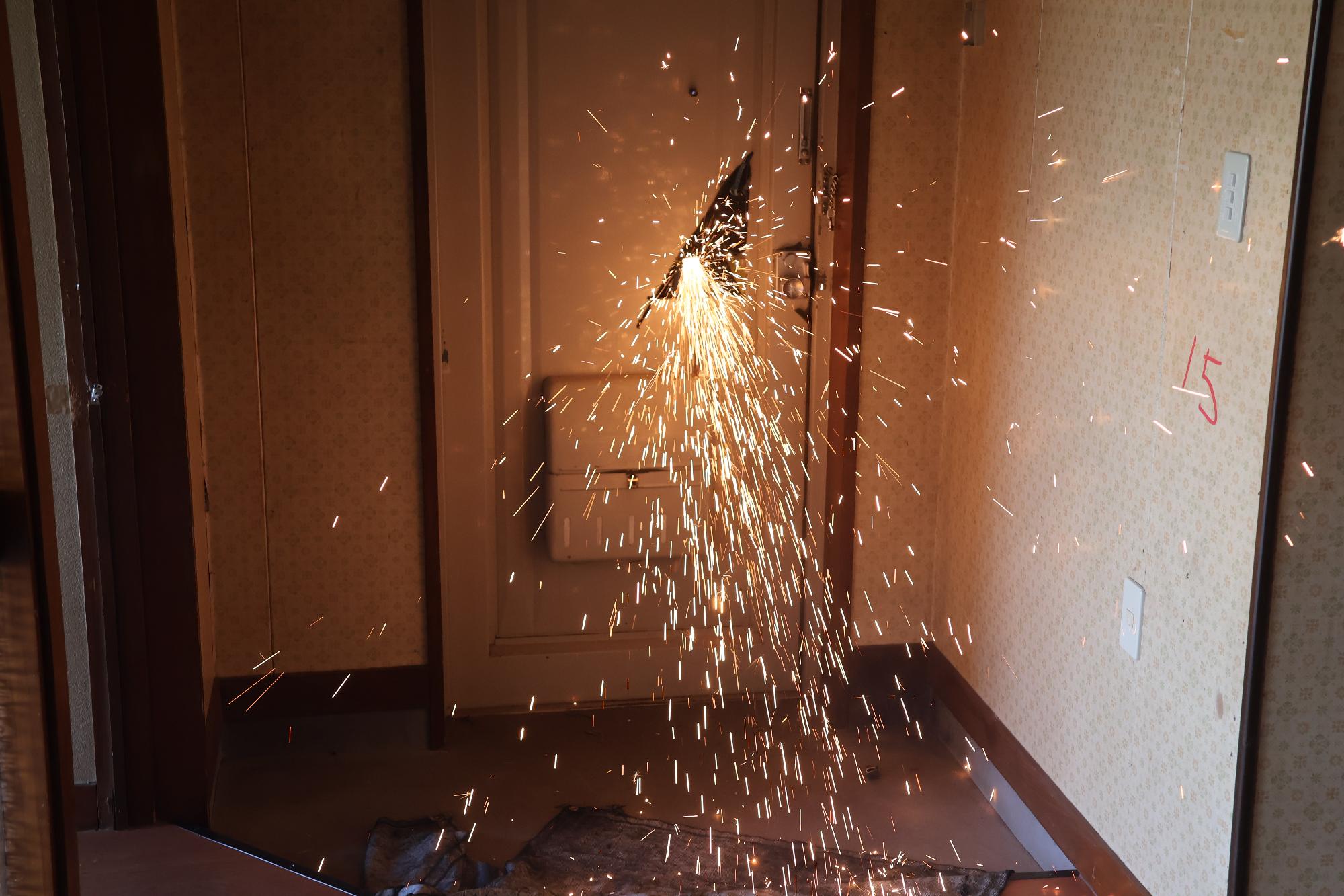 鉄の扉を救助隊員がエンジンカッターで火花を散らしながら切断している様子を室内から撮影した写真