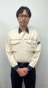紺色の襟と袖口のラインが入ったクリーム色の作業服を着用し、眼鏡をかけた男性が、両手を体の前で組んでカメラに向かってまっすぐ立っているお客さまセンター職員の服装の一例の写真
