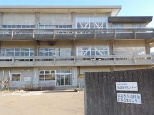 手前に「福島市水道料金お客さまセンター」と書かれた看板がある薄灰色のコンクリート造りの建物正面をとらえた写真