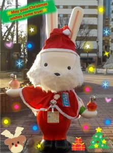 「May your Christmas wishes come true!」の文字と星や雪、クリスマスツリー、トナカイなどの装飾的なエフェクトが施され、赤いサンタクロースの衣装と帽子を身に着けて街中に立つももりんウォーターの写て