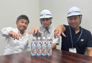 テーブルに福島市の水道水「ふくしまの水」のけっぱって東北ver.コラボデザインのボトルが3本並べられて、作業服姿の3人の男性が手のひらを下に向けるポーズをとって写っている写真