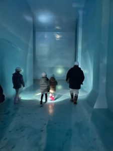 全体が薄い青色で照らされたトンネル状の空間を、ヘルメットを着用した大人1人と子ども3人が足元を照らしながら奥へ進んでいる様子を写した、中央部受水池の内部の写真