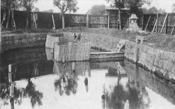 石垣に囲まれた水面に水が満ちた柳清水水源地と、水中に立つ杭や木製の構造物が当時の貴重な水源の様子を伝える柳清水水源のモノクロ写真