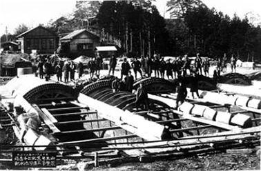 円弧状の巨大な蓋の骨組みのようなものが配置され、その周囲で多数の作業員が作業している様子を撮影したモノクロ写真