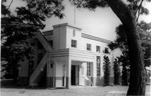 周囲を松の木などの樹木に囲まれた、直線的なデザインと平らな屋根を持つ清水水源ポンプ所の外観モノクロ写真