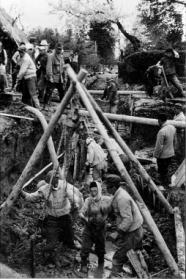 斜面の崩れやすい地面に木材を組んで足場を設け、多数の作業員が泥まみれになりながら、土砂を掘削したり資材を運んだりしている当時の工事風景をとらえたモノクロ写真