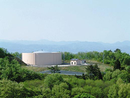 山の稜線を見渡す高台の樹木に囲まれた空間に、薄茶色の円形で巨大な配水池と、その手前に建つ小さな管理棟のような建物が配置されている南部受水池の写真