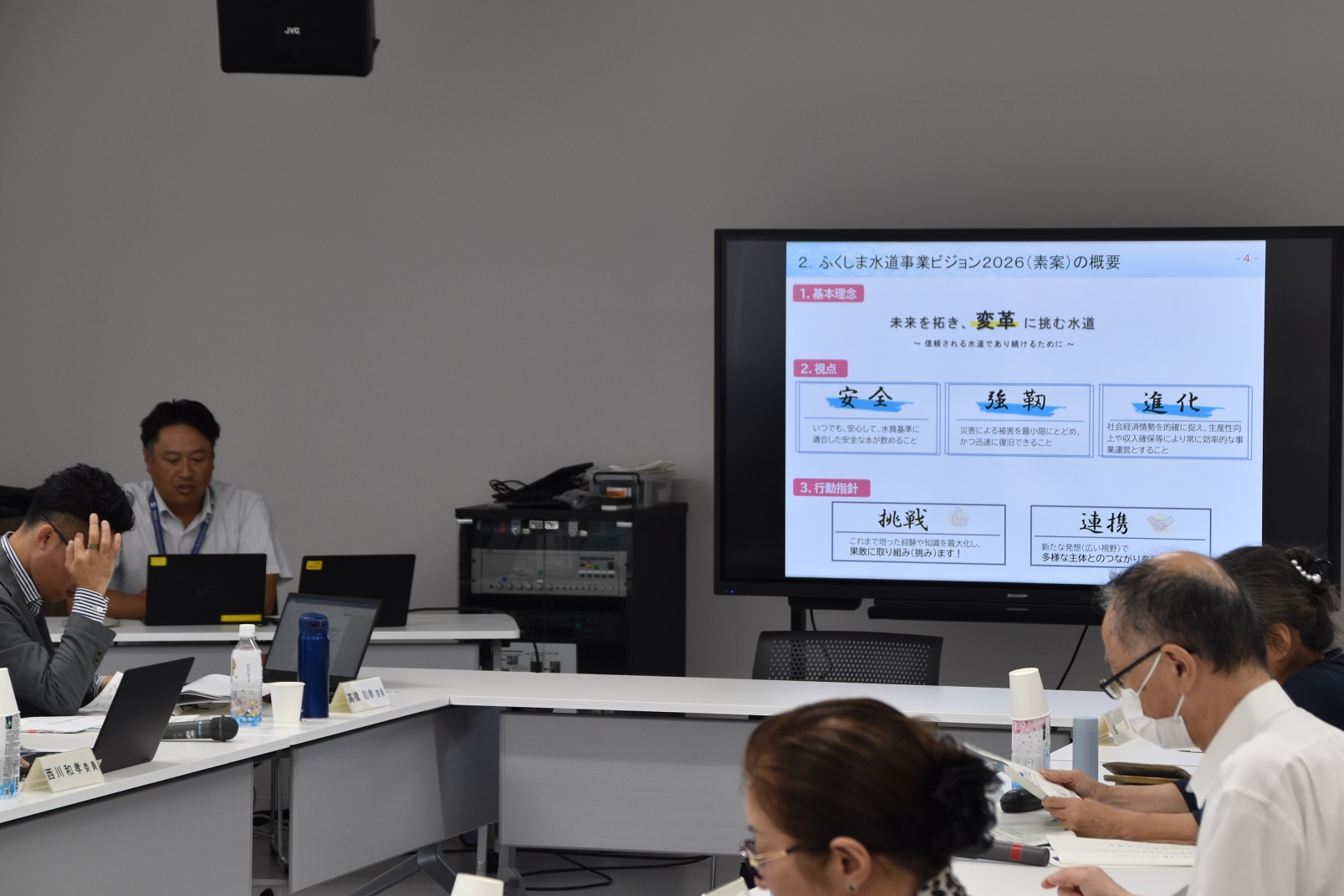 ディスプレイに表示された議題や手元にある資料を見ながら議論を行っている会議風景の写真