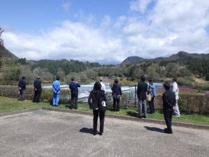 晴れた日に、数名の関係者が広々とした駐車場のような場所からすりかみ浄水場施設を眺めている様子を背後から撮影した写真