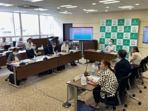 複数のテーブルをコの字型に配置し、部屋の奥には福島市のバックボード、両側にモニターが設置された会議室で多くの参加者が着席して資料を眺めたり同じ方向を向いている会議風景の写真