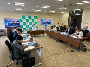 複数のテーブルをコの字型に配置し、部屋の奥には福島市のバックボード、両側にモニターが設置された会議室で多くの参加者が着席している会議風景の写真
