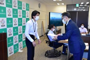 福島市のバックボードのそばで清野一浩水道事業管理者から齋藤寛礼委員に委嘱状を渡している様子の写真