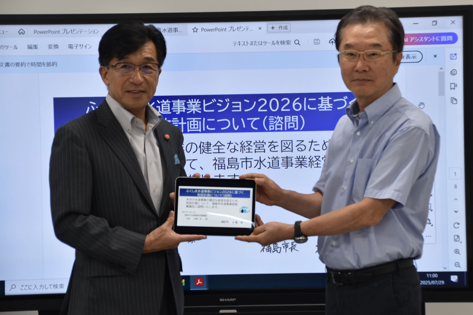 市長と関係者の男性が「ふくしま水道事業ビジョン2026に基づく財政計画について（諮問）」と表示されているタブレット画面を一緒に持って記念撮影を行っている様子の写真