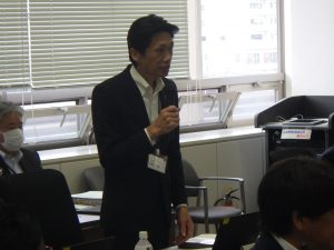 関係者の男性がマイクを片手に話をしている様子の写真