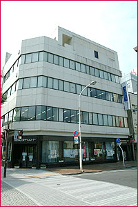 交差点に建つ5階だての白い外壁で窓がたくさんある男女共同参画センターの外観を写した写真